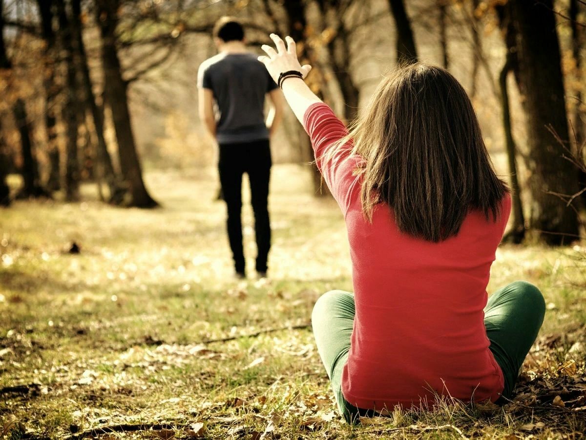 Woman seated outdoors reaching toward a man walking away.