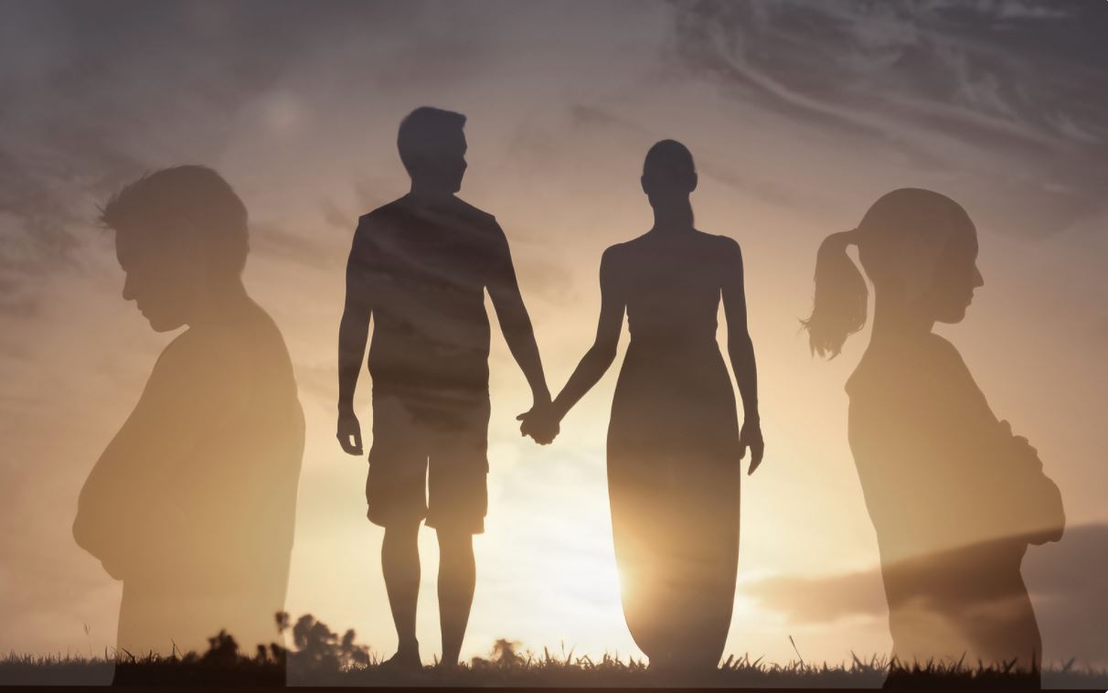 Silhouettes of a couple holding hands at sunset, with larger side-profile silhouettes behind them.